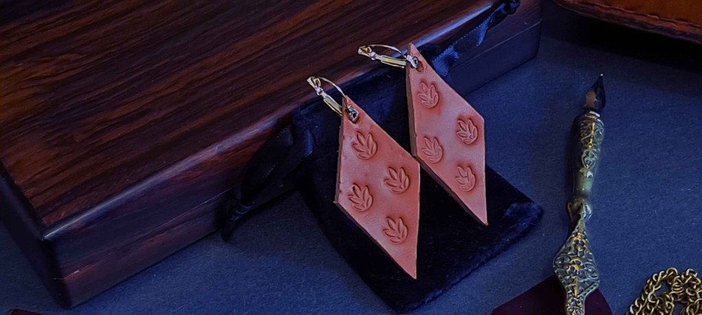 Colección: El Oráculo de la Tierra – Relieve Ancestral
Donde la Paciencia deja su Huella Eterna

Existe un lenguaje anterior a las palabras. Es el lenguaje del tacto, del relieve, de la huella que perdura. Esta colección nace del diálogo sagrado entre el agua, el tiempo y la mano.
Aquí no hay prisa. Solo el ritual paciente de humedecer el cuero virgen —ablandando su resistencia— para luego entregarlo al golpe preciso del sello. Cada impacto no es violencia; es una conversación. La presión calculada no corta, modela. No es un dibujo en la superficie; es una memoria grabada en la profundidad.

Estos pendientes no fueron hechos solo para ser vistos. Fueron creados para ser sentidos. Pasan los dedos sobre ellos y leerás la historia de su creación: aquí la curva suave de una semilla, allí el vértice de una figura diminuta. Su relieve es un mapa topográfico para el alma, una invitación a recordar que la verdadera belleza no brilla, reside.

Llévalos en los días en que el mundo exige velocidad y tú anhelas calma. En los momentos en que necesitas recordar que eres de raíz y sustancia, no de apariencia. Son tu recordatorio portátil de que las cosas más sólidas —el carácter, la paz, la sabiduría— se forjan con presión paciente, no con fuego rápido.

Colección «Relieve Ancestral»: Para quienes buscan belleza con raíces.

Hecho para durar, hecho para sentir.

Técnica: Repujado artesanal en cuero húmedo.
Material: Cuero vegetal de primera calidad.
Herrajes: Alpaca/níquel libre.
Medidas: Alto: 6 cm, Ancho 2 cm.
Condición: Nuevo, hecho a mano